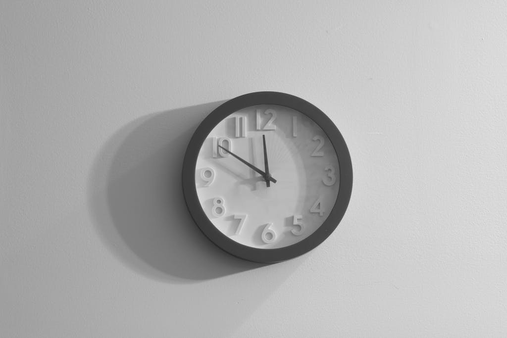 A black and white wall clock casting a shadow against a plain wall.