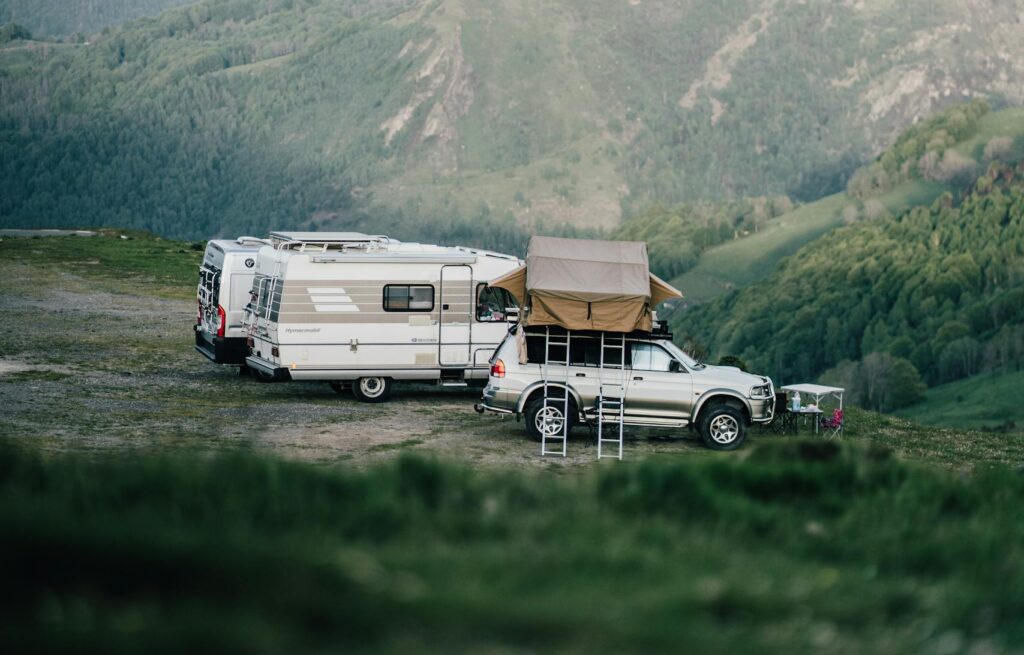 A car and camper van set up camp in a serene mountainous landscape, perfect for an adventurous escape.